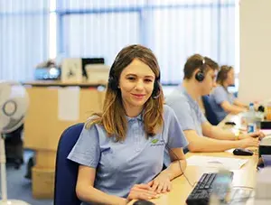 Natural Pharmaceuticals Melatonina Moteris su ausinėmis dirba klientų aptarnavimo centre biure, šalia jos kolegos toje pačioje darbo vietoje.