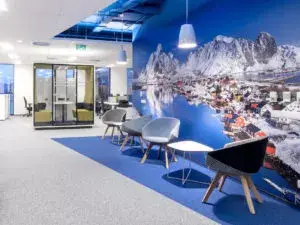 Natural Pharmaceuticals Melatonina Modernaus ofiso poilsio zona su kėdėmis ir stalu prie sienos su kalnų ir ežero peizažo freska.