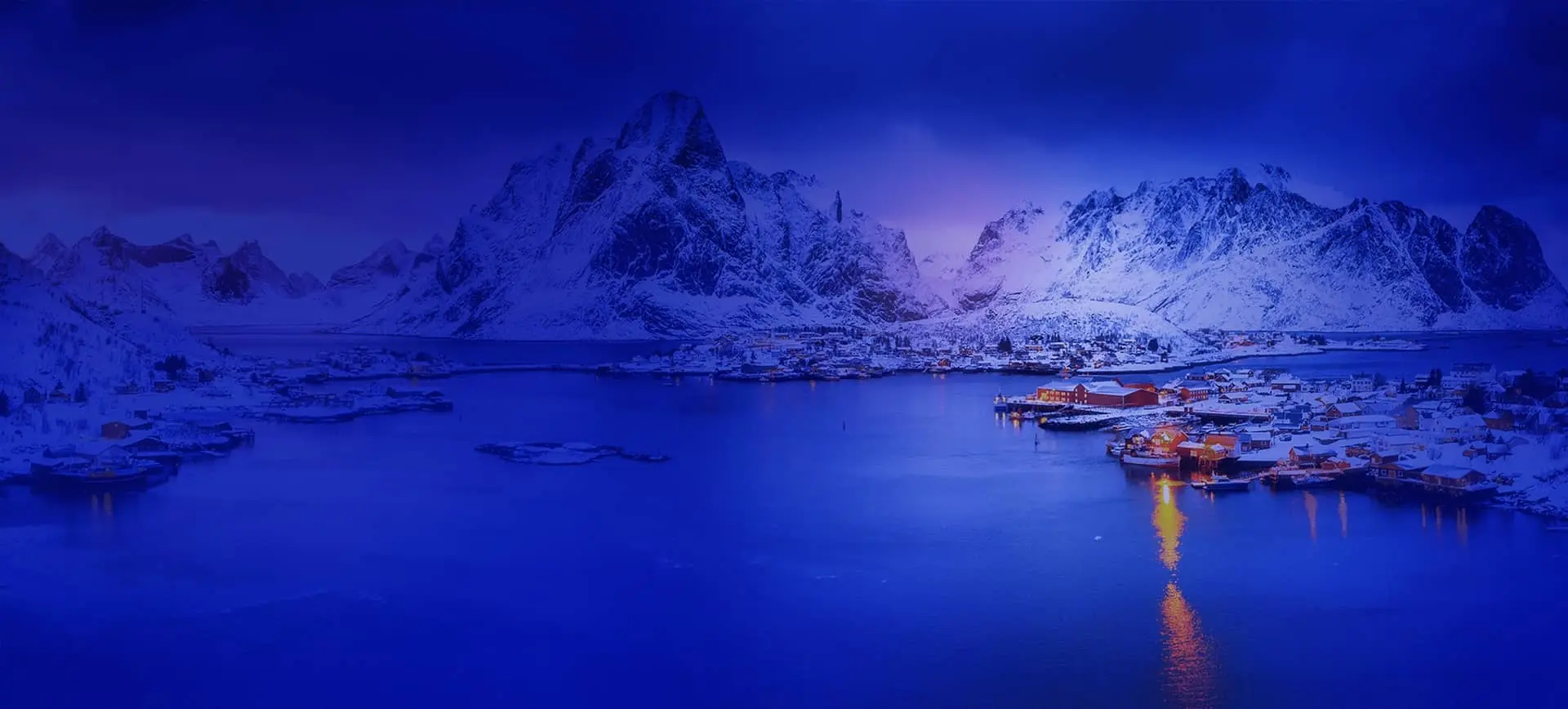 Natural Pharmaceuticals Melatonina Naktinis snieguotas kalnų miestelis prie ramios įlankos su šiltu apšvietimu ir tamsiai mėlyna dangumi.