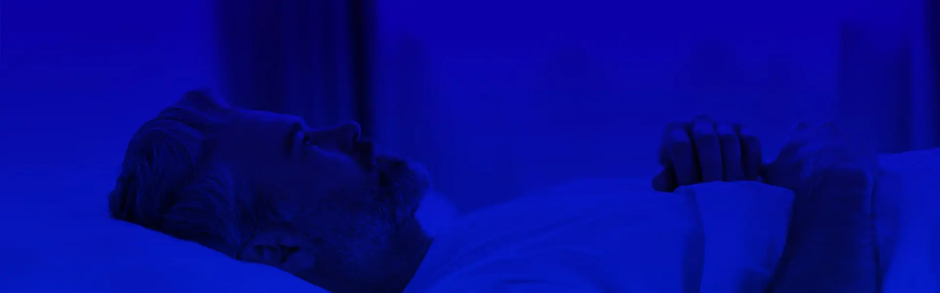 Natural Pharmaceuticals Melatonina Vyras guli lovoje ir negali užmigti tamsiame kambaryje mėlyno apšvietimo sąlygomis.